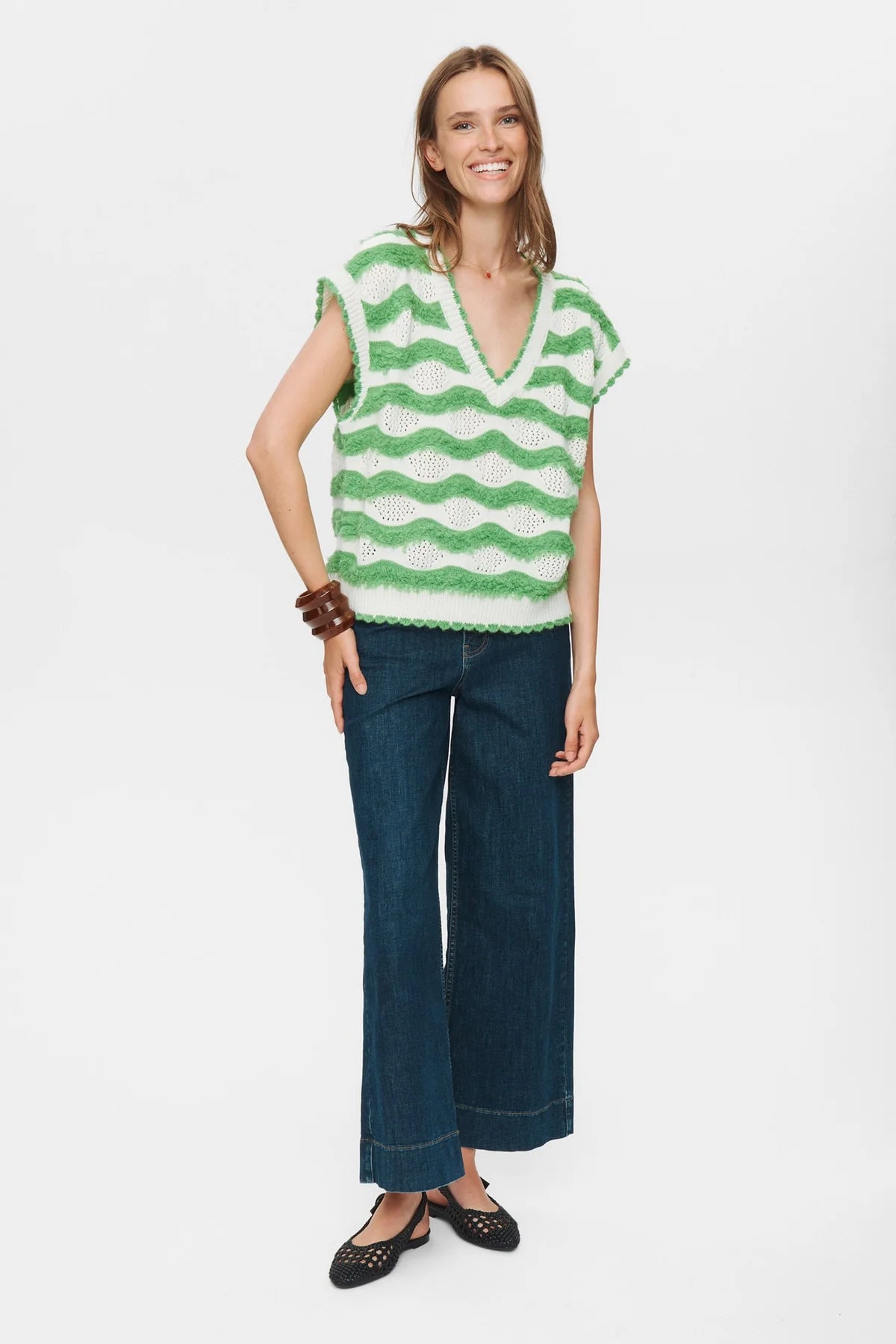 Woman wearing a green and white striped sleeveless top with blue jeans on a white background