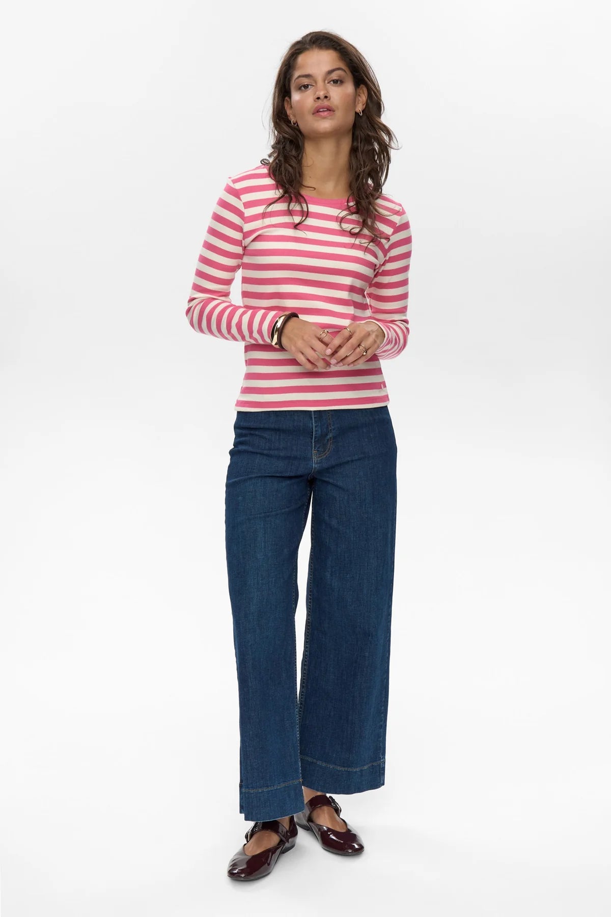 Woman wearing a pink and white striped shirt and blue jeans on a white background