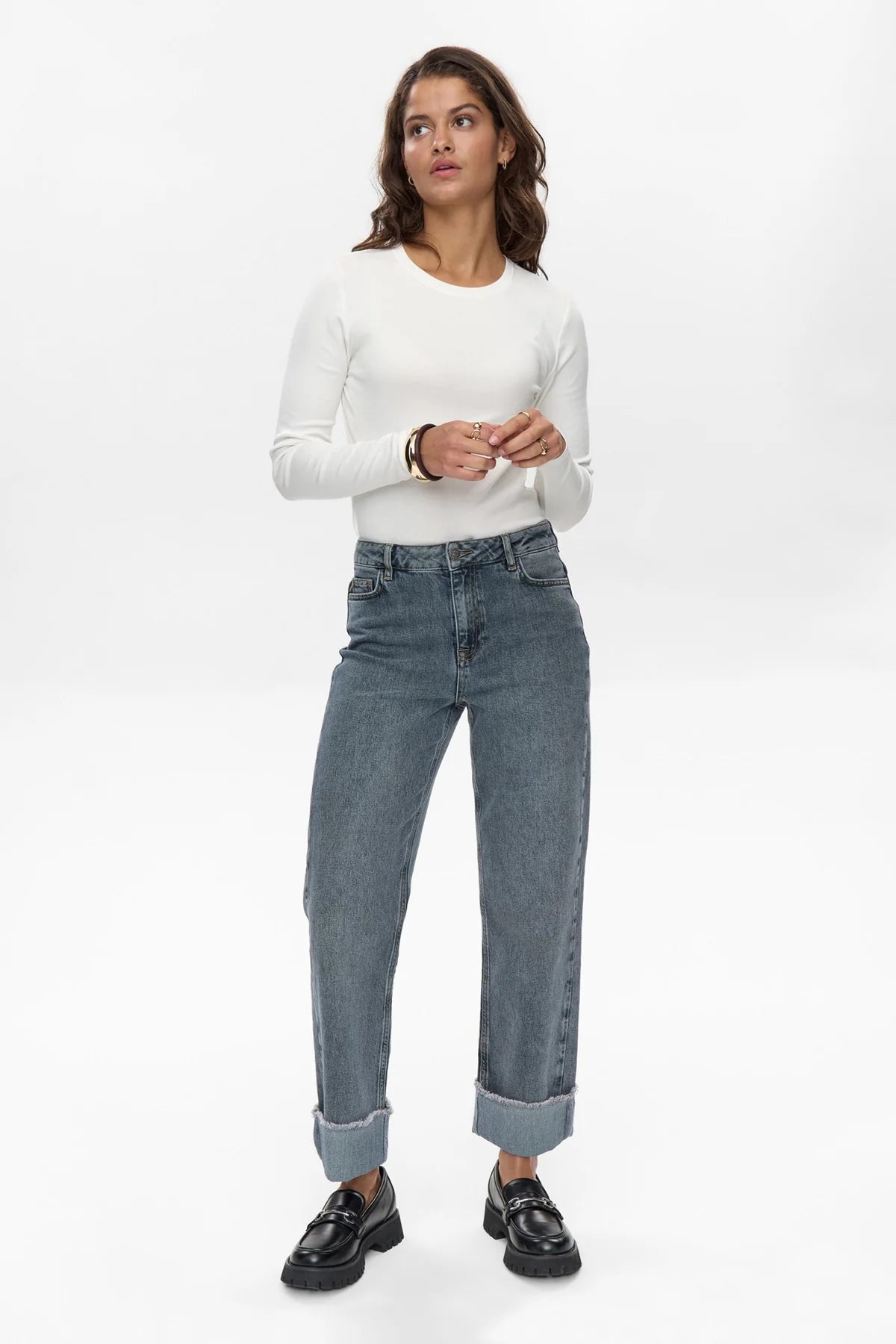 Woman wearing a white long-sleeve top and blue jeans on a white background