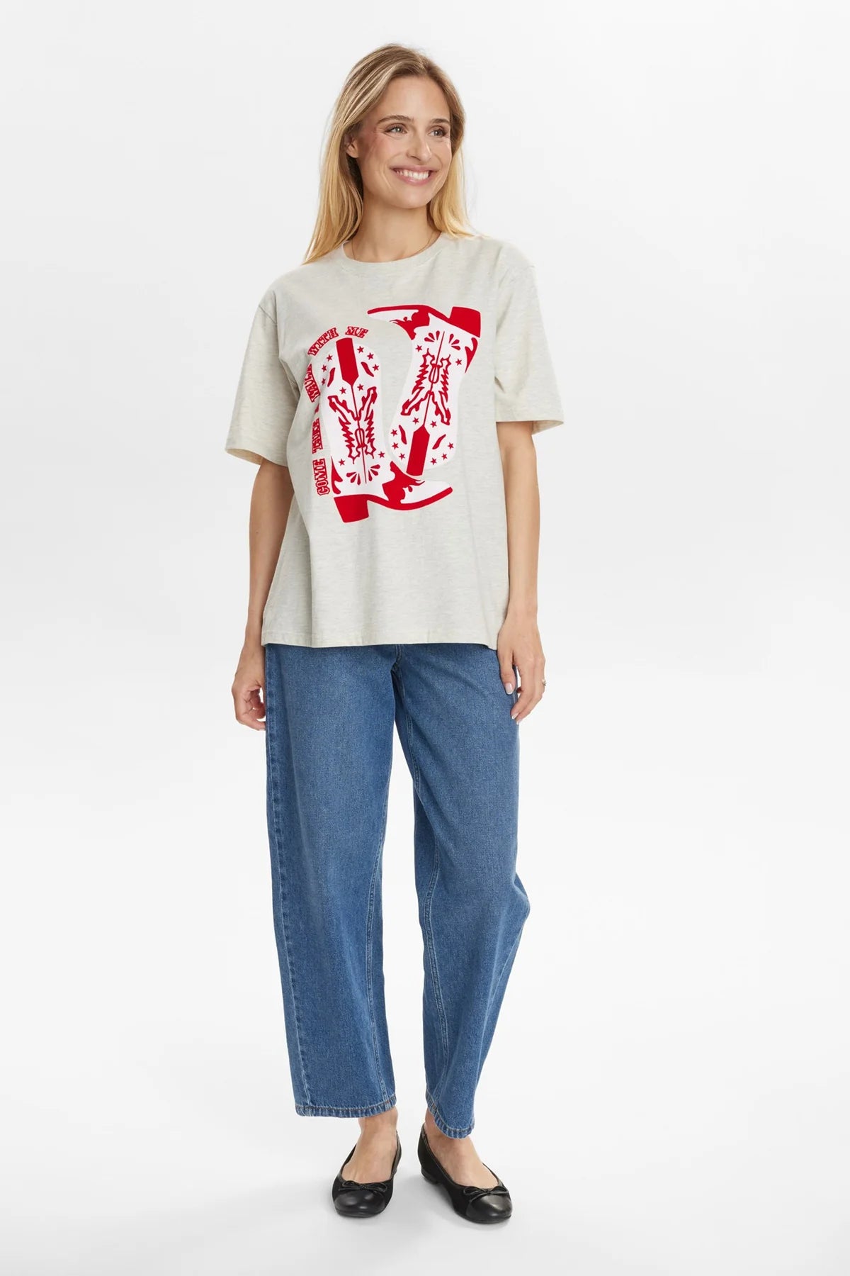 Woman wearing a cream t-shirt with red graphic and blue jeans on a white background