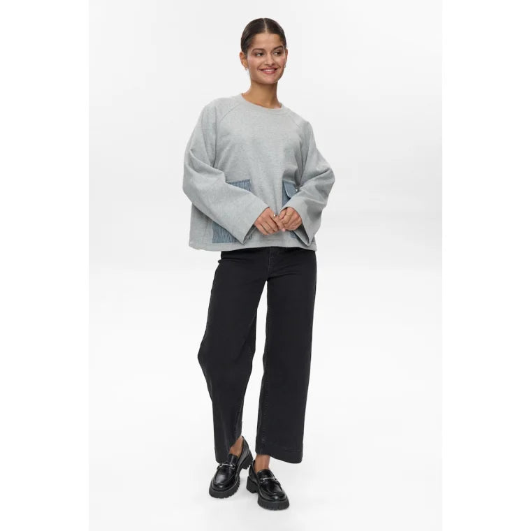 Woman wearing a grey sweater and black pants on a white background