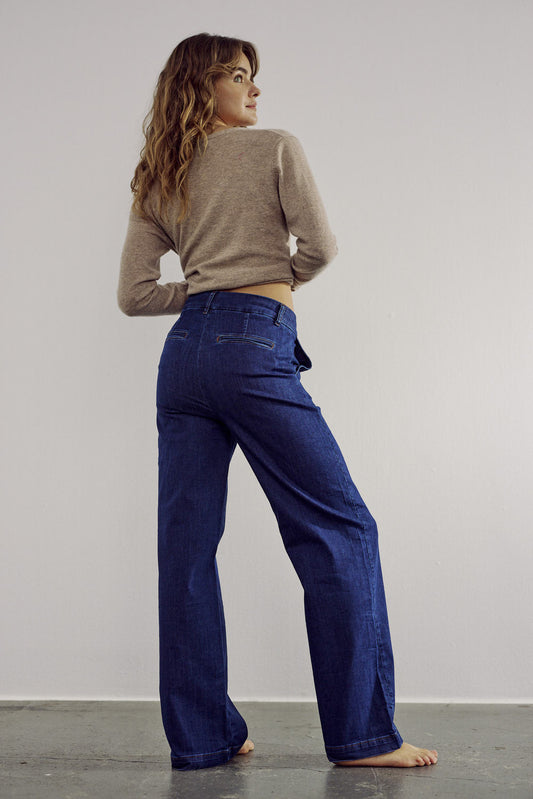 Woman wearing a beige sweater and blue jeans against a plain background