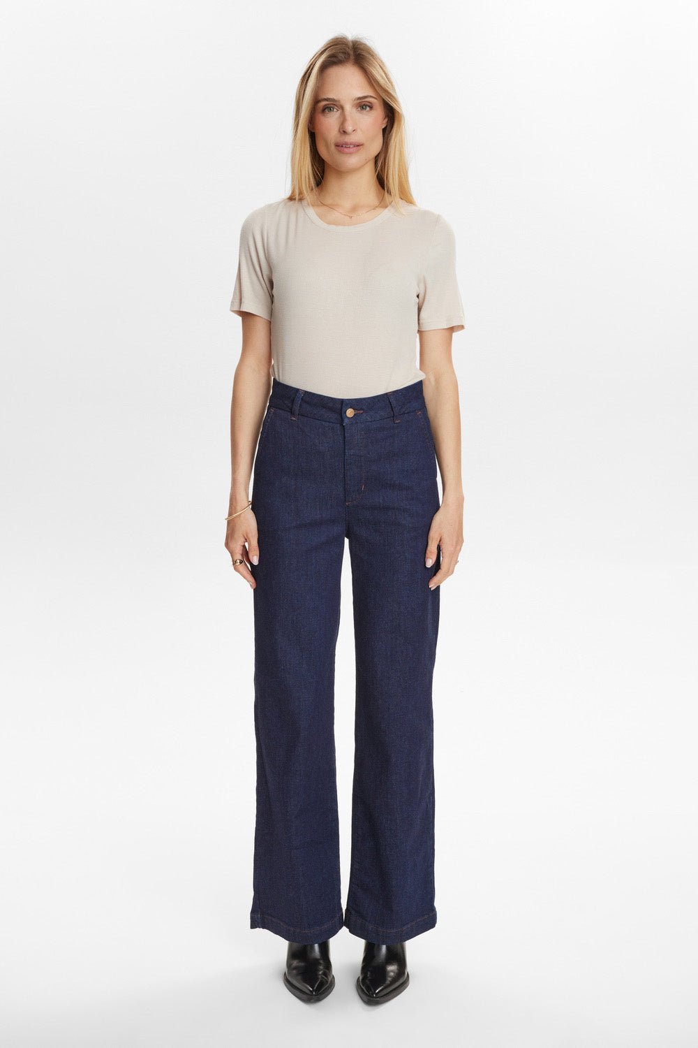 Woman wearing a beige t-shirt and dark blue jeans on a white background