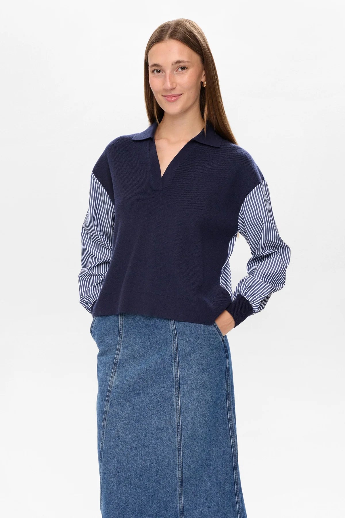 Woman wearing a navy sweater with striped sleeves and a denim skirt on a white background