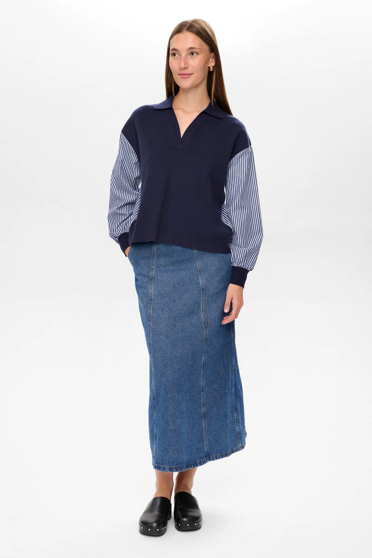 Woman wearing a navy sweater with a striped pattern and a long blue denim skirt on a white background