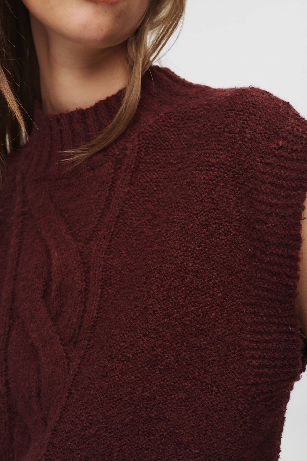 Close-up of a person wearing a burgundy knitted sleeveless sweater against a neutral background