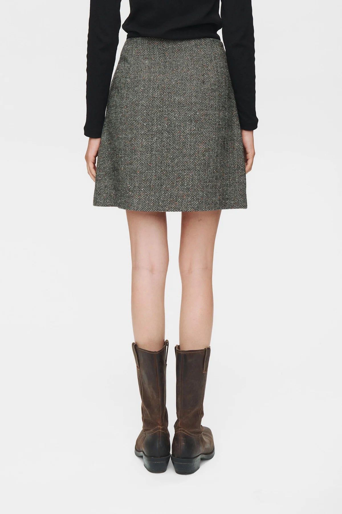Person wearing a gray skirt with brown boots on a white background