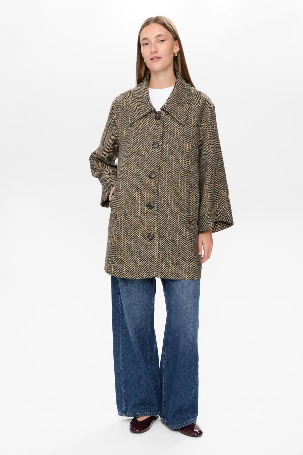 Woman wearing a tweed coat and blue jeans on a white background