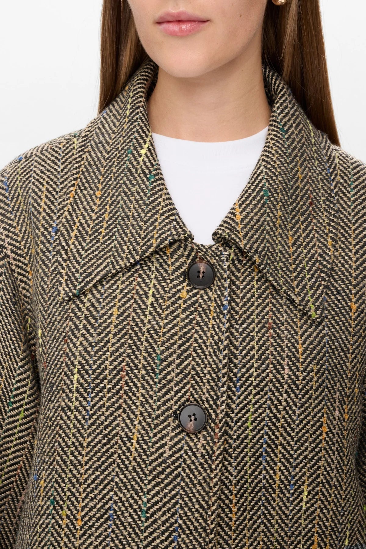 Close-up of a person wearing a herringbone patterned coat with a white shirt underneath.