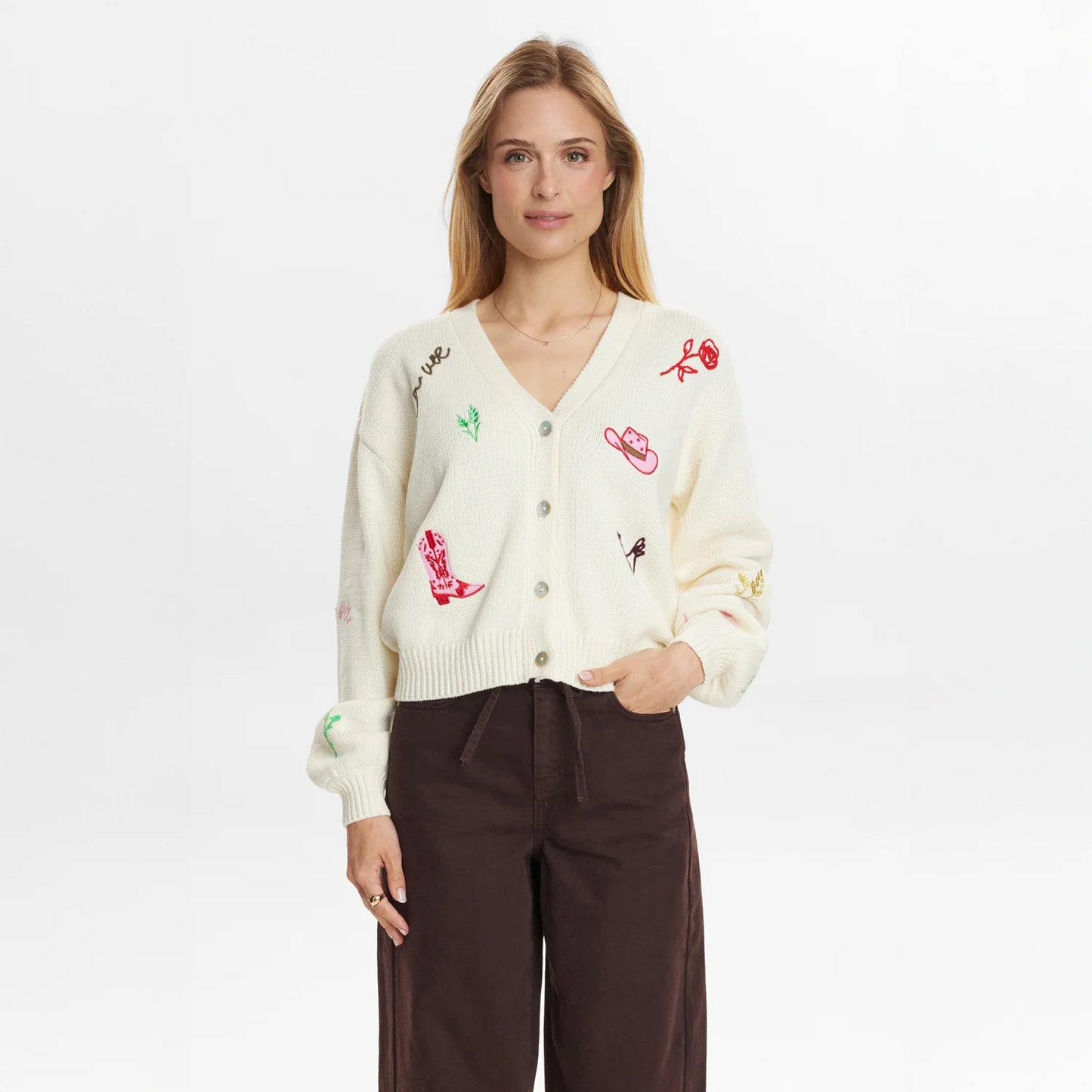 Woman wearing a cream cardigan with colorful embroidery on a white background