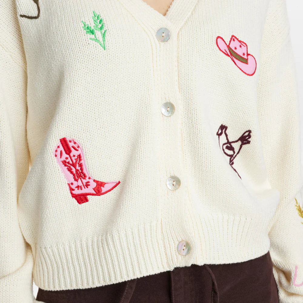 White cardigan with colorful embroidered designs on a plain background
