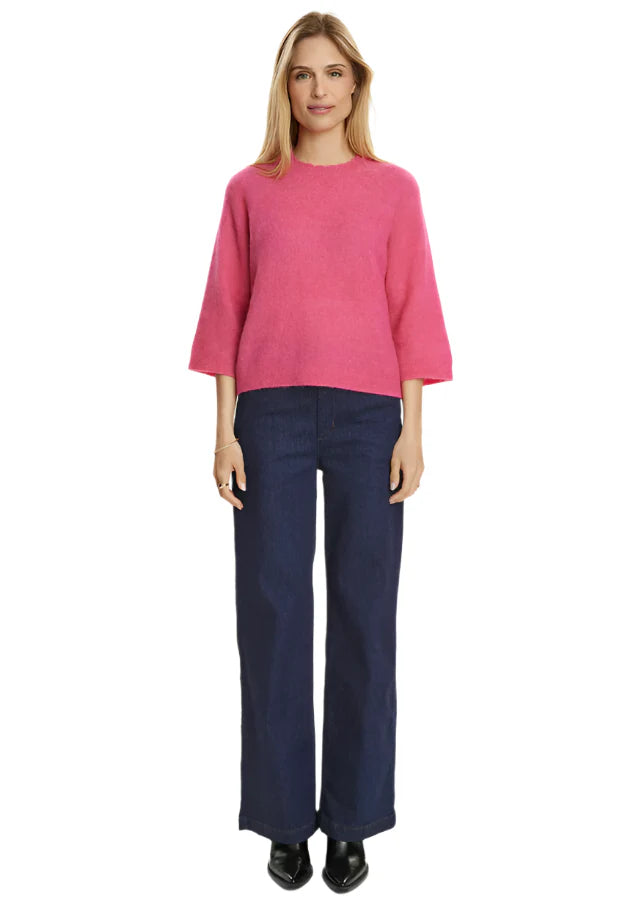 Woman wearing a pink sweater and navy pants on a white background