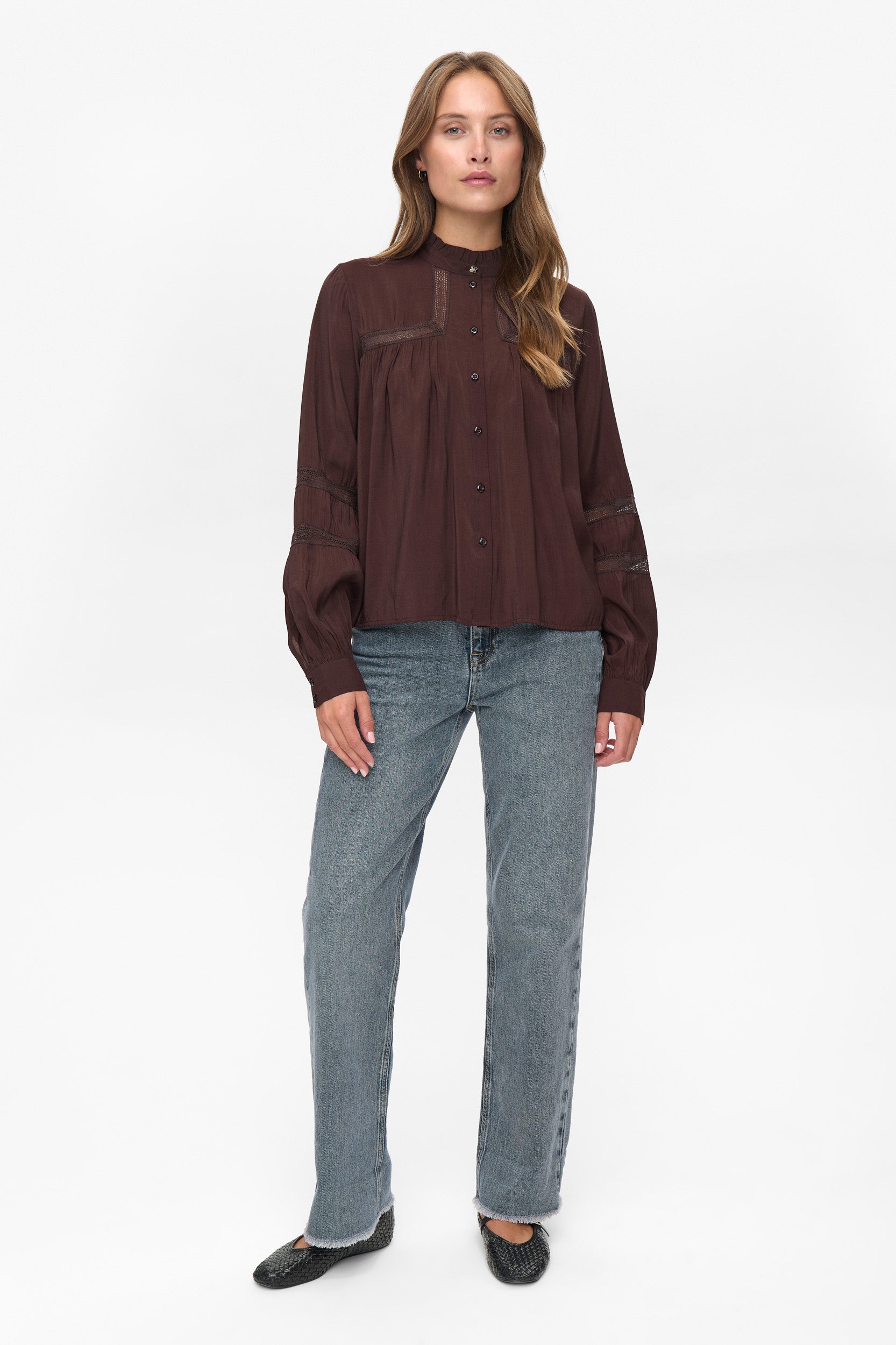 Woman wearing a brown button-up shirt and blue jeans on a white background