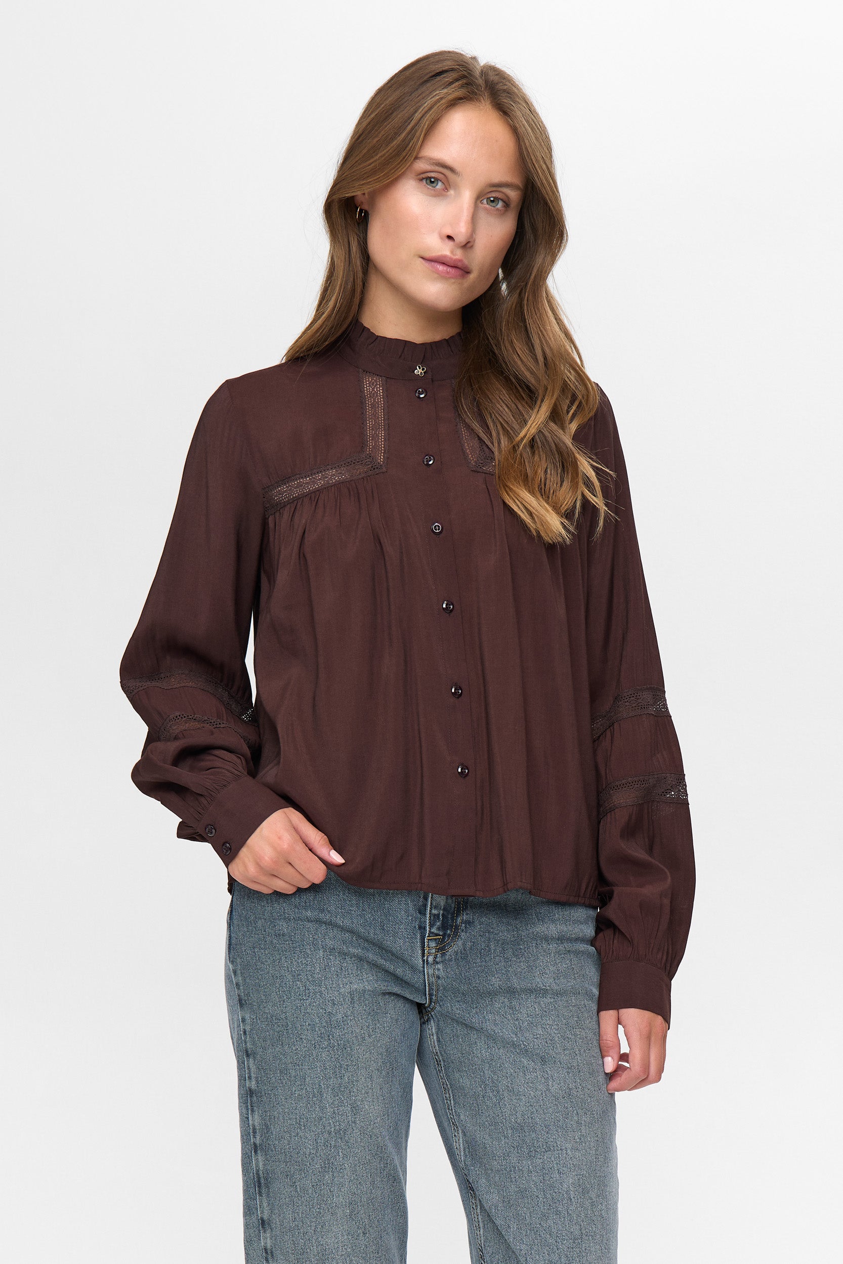 Woman wearing a brown blouse with sheer panels and blue jeans on a white background