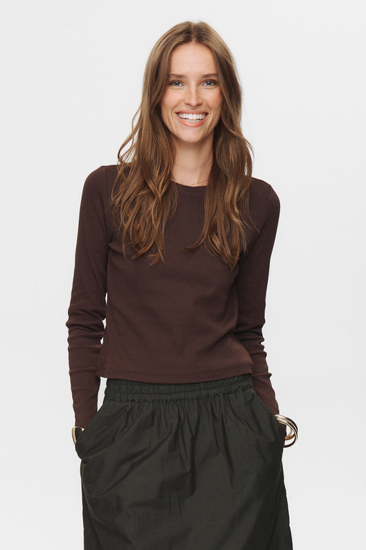 Woman wearing a brown long-sleeve top and black pants on a white background