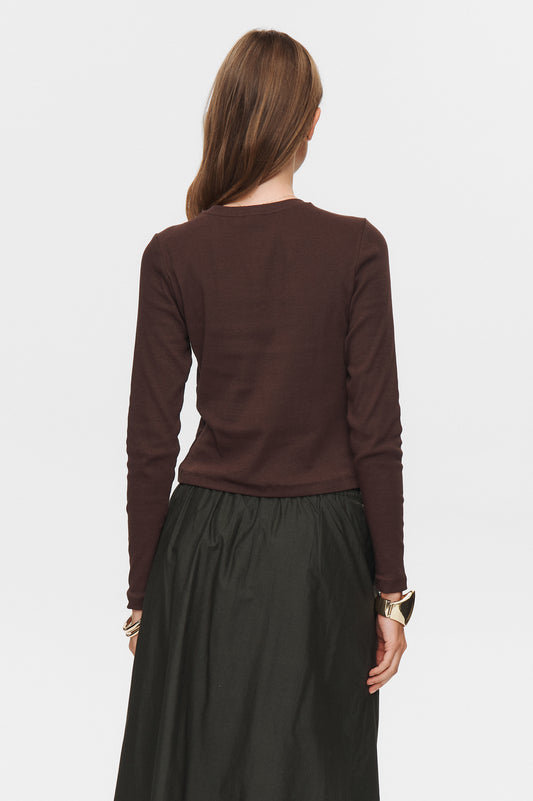 Person wearing a brown long-sleeve top and dark skirt on a white background