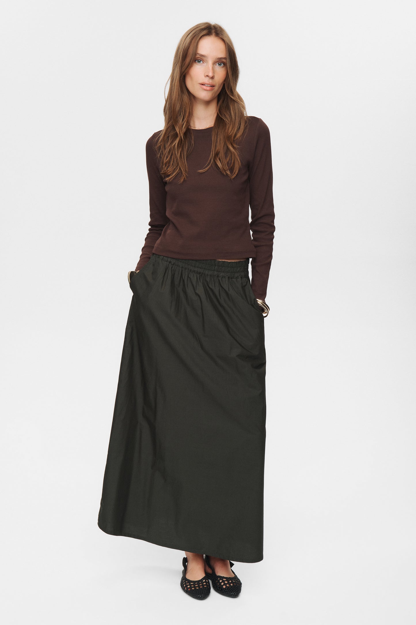 Woman wearing a brown top and long dark green skirt on a white background