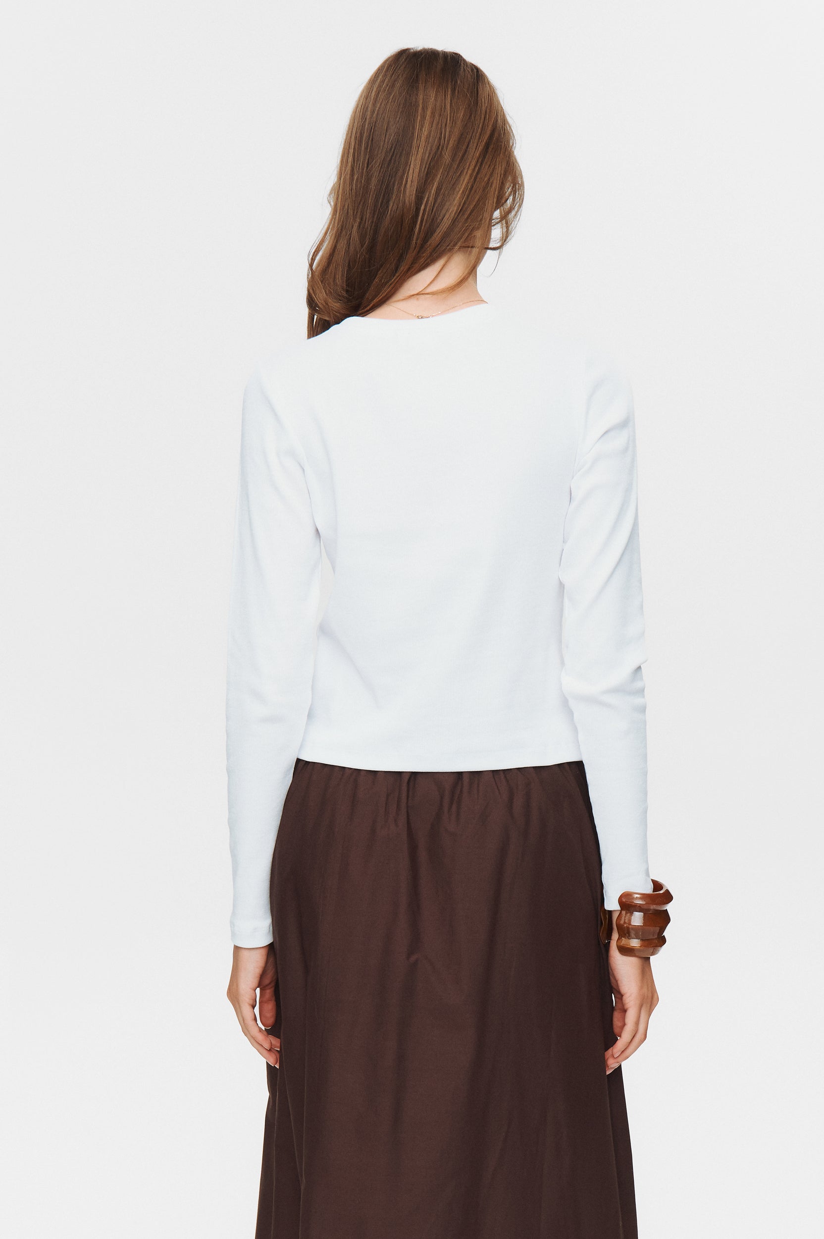 Person wearing a white long-sleeve shirt and brown pants on a white background