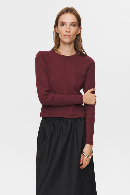 Woman wearing a burgundy long-sleeve top and black skirt on a white background