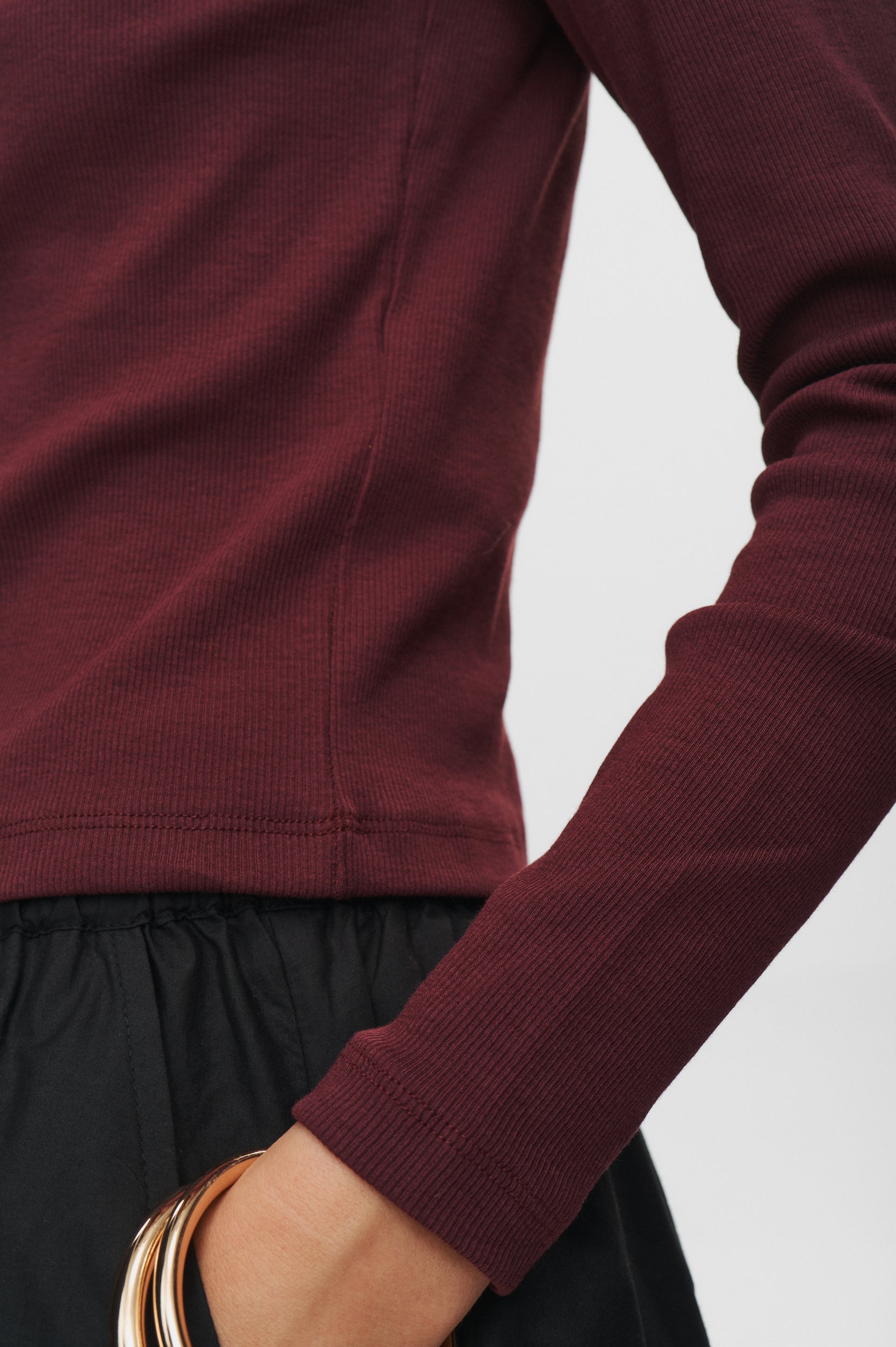 Close-up of a person wearing a burgundy long-sleeve top with a plain background