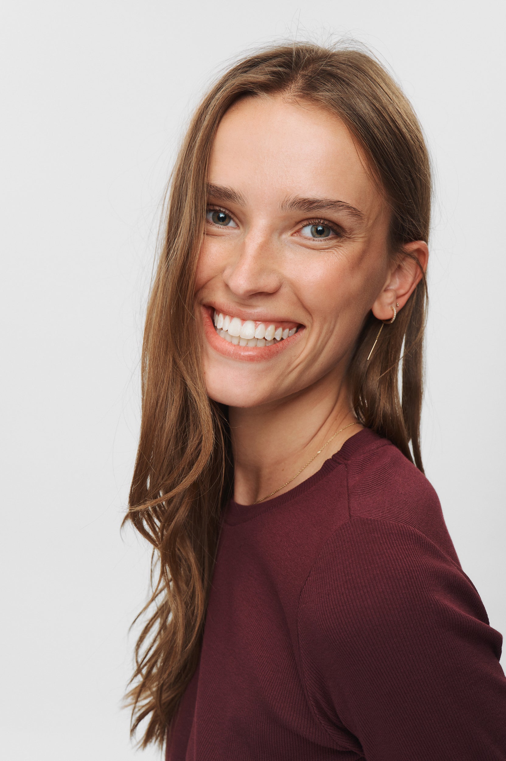 Woman with long brown hair wearing a maroon shirt against a white background