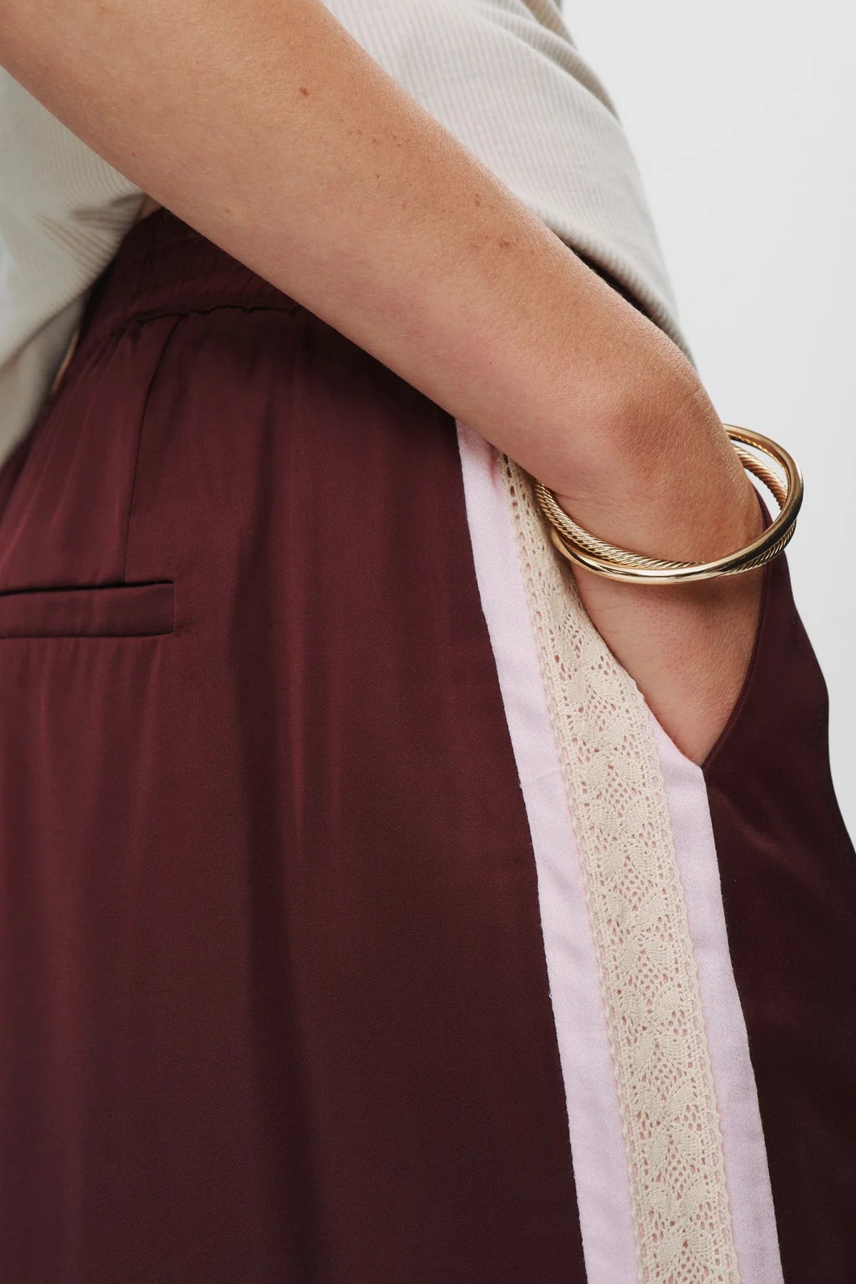 Close-up of a person wearing a gold bracelet on a plain background