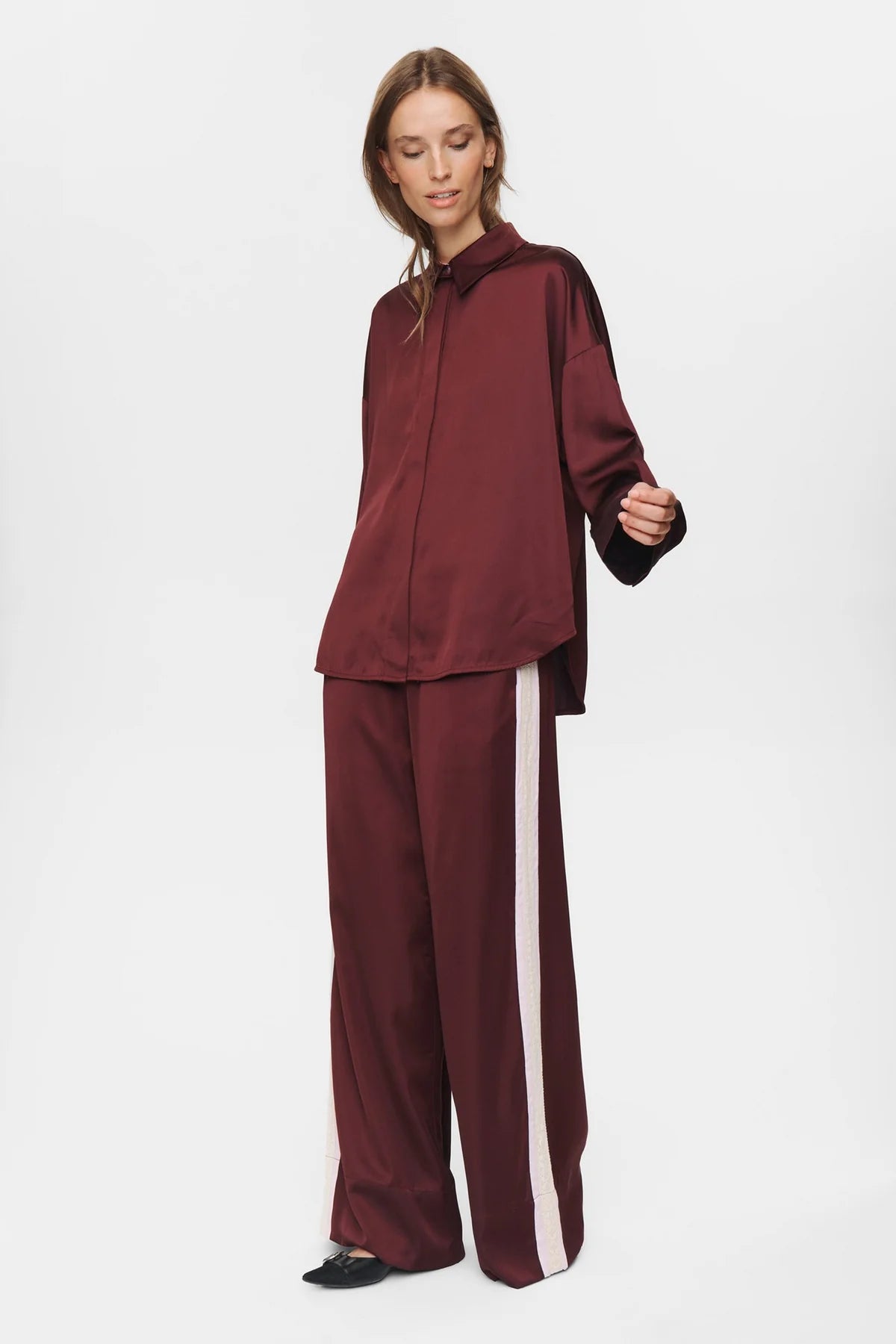 Woman wearing a burgundy tracksuit with a white stripe on a white background