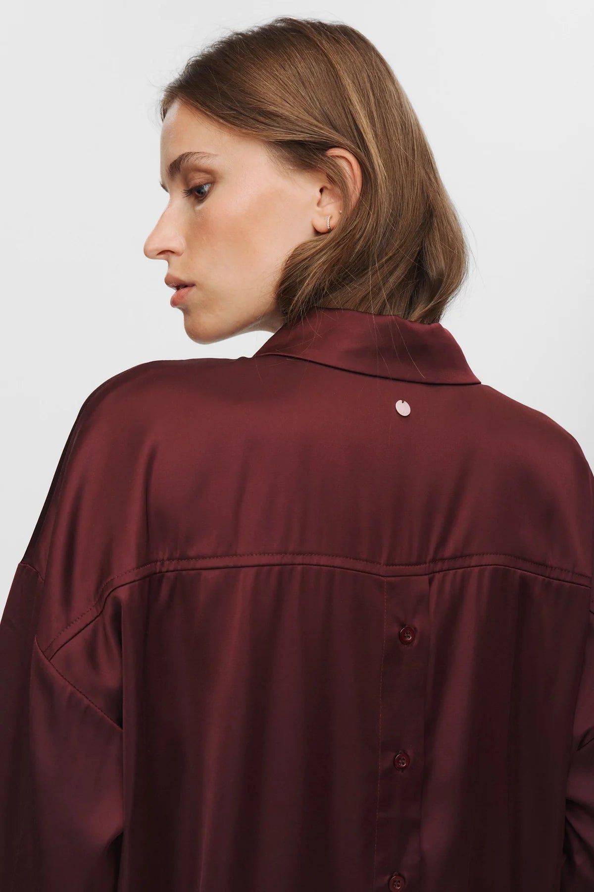 Person wearing a burgundy satin shirt on a plain background