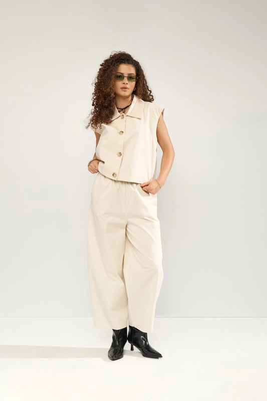 Person wearing a cream sleeveless jacket and pants with black boots on a white background