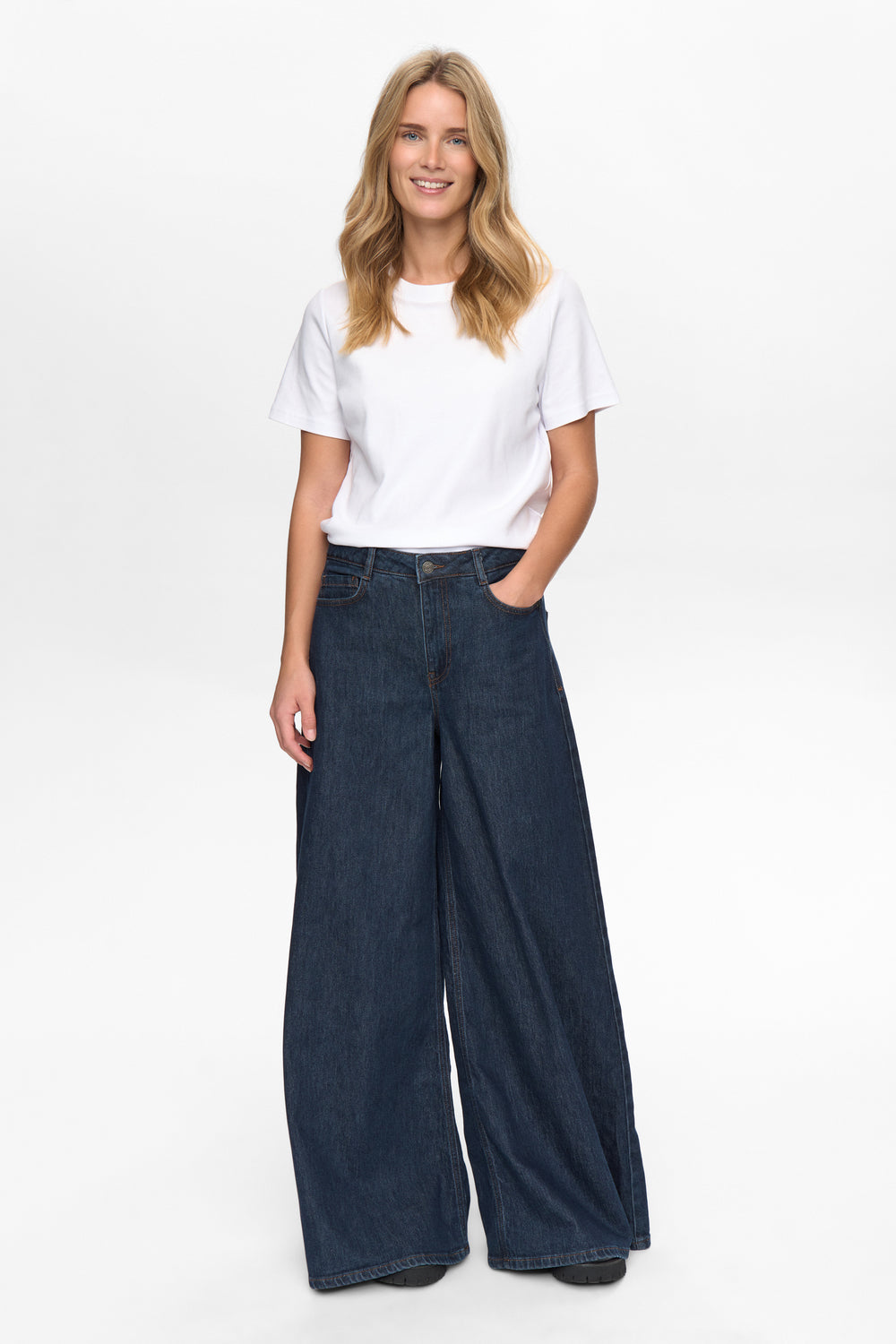 Woman wearing a white t-shirt and dark blue wide-leg jeans on a white background