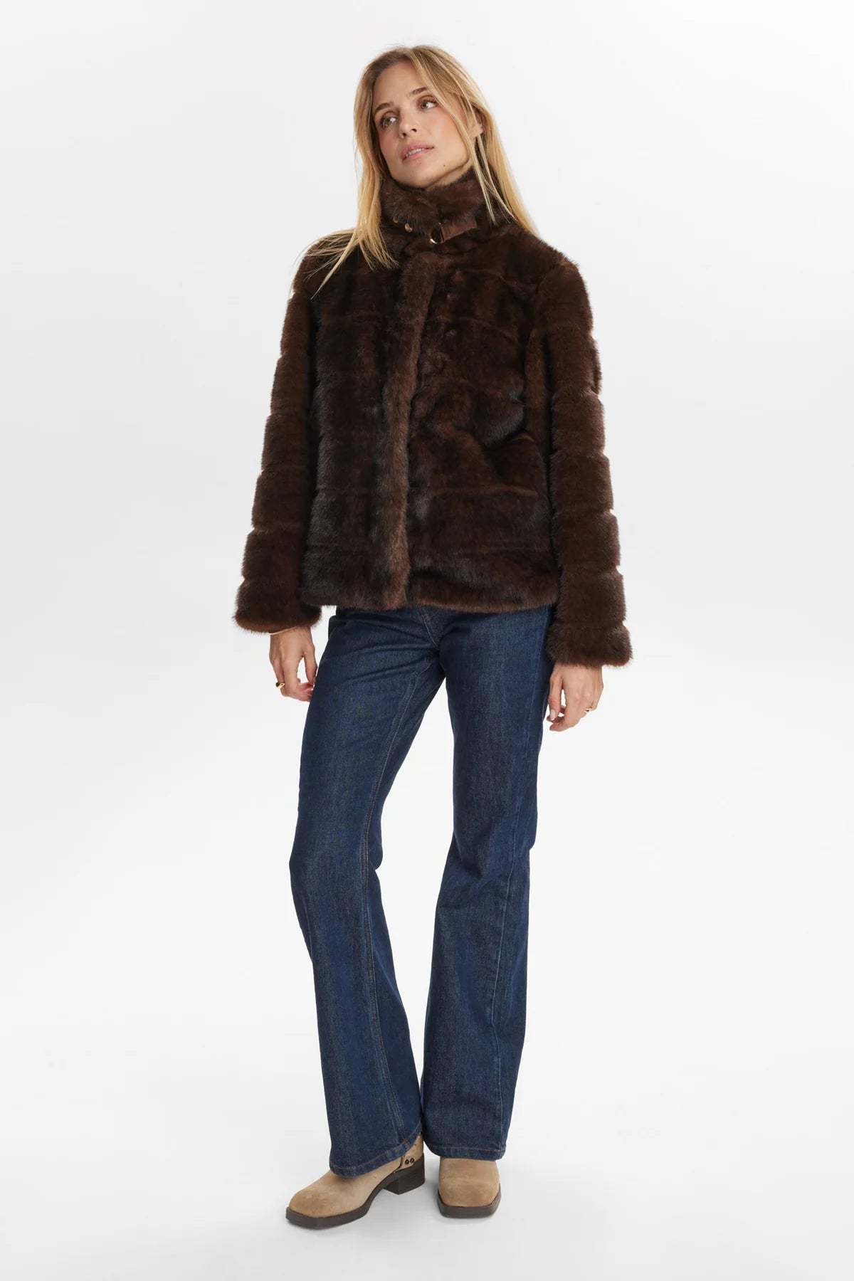 Woman wearing a brown fur coat and blue jeans on a white background