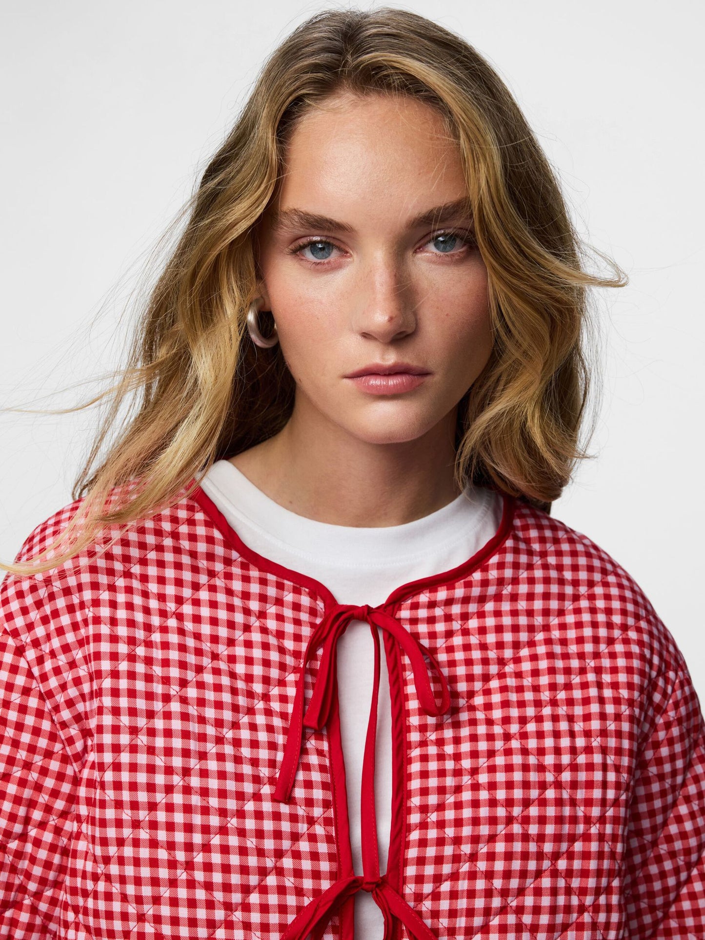 Woman wearing a red and white checkered blouse with a white collar against a light background