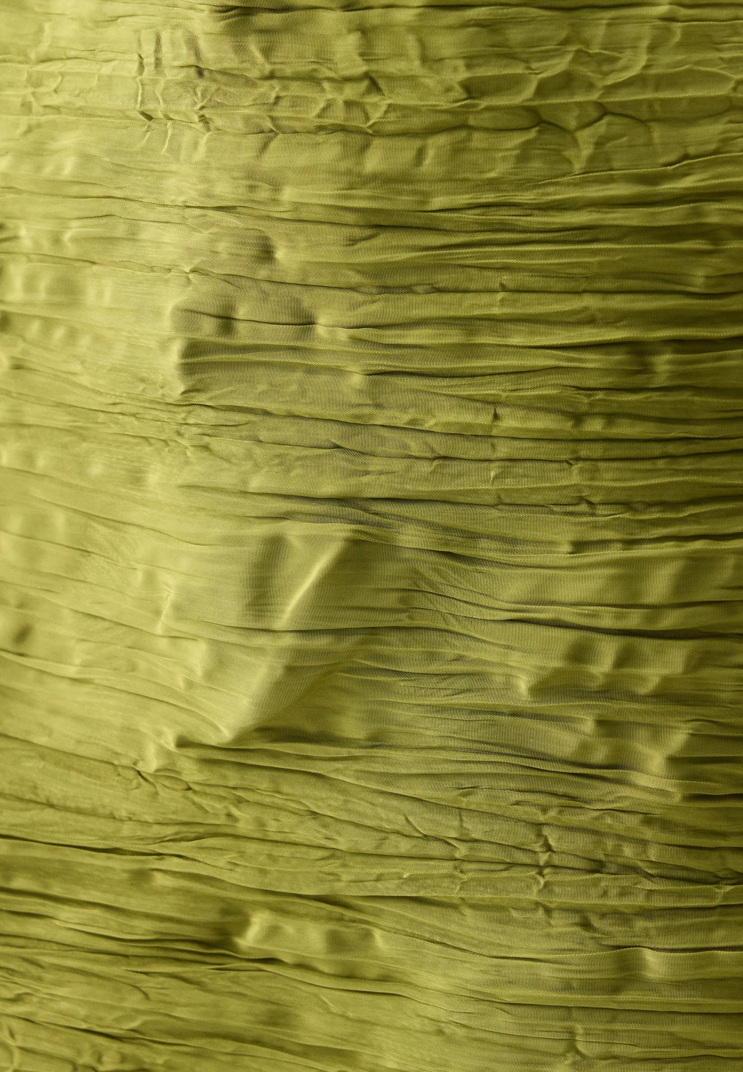 A close-up of olive green crinkled paper or textured fabric with horizontal folds and a slightly translucent surface.