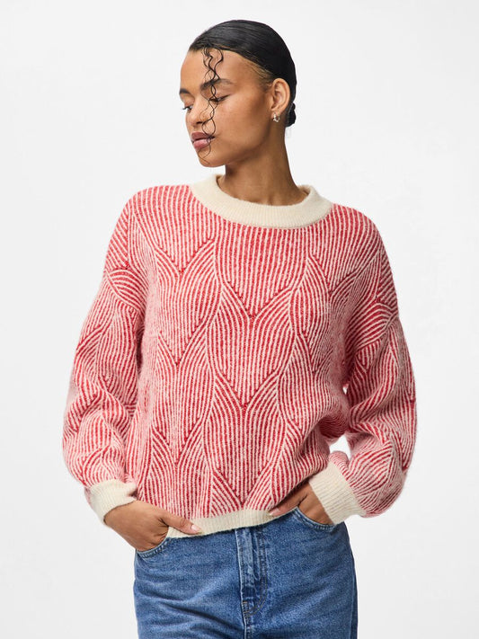 Person wearing a red and white patterned sweater with blue jeans on a plain background