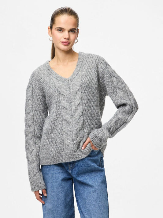Woman wearing a gray cable knit sweater and blue jeans on a white background