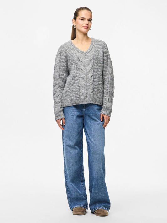 Woman wearing a gray cable knit sweater and blue jeans on a white background