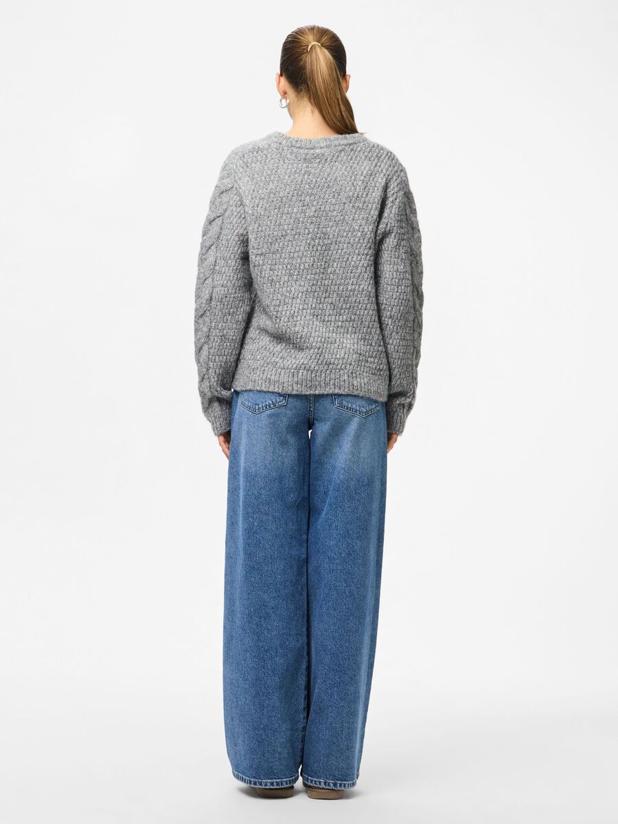 Person wearing a gray textured sweater and blue jeans on a white background