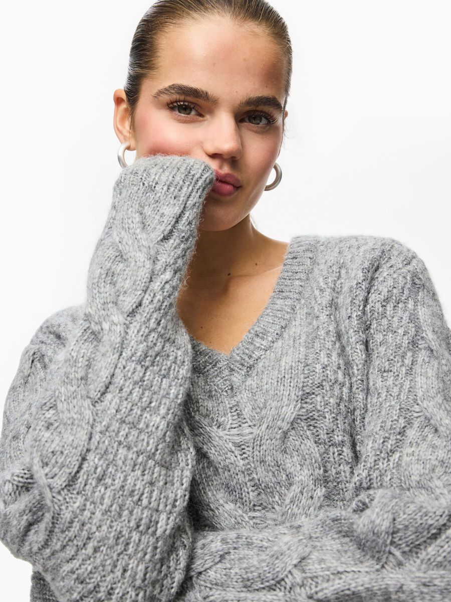 Woman wearing a gray cable knit sweater on a white background