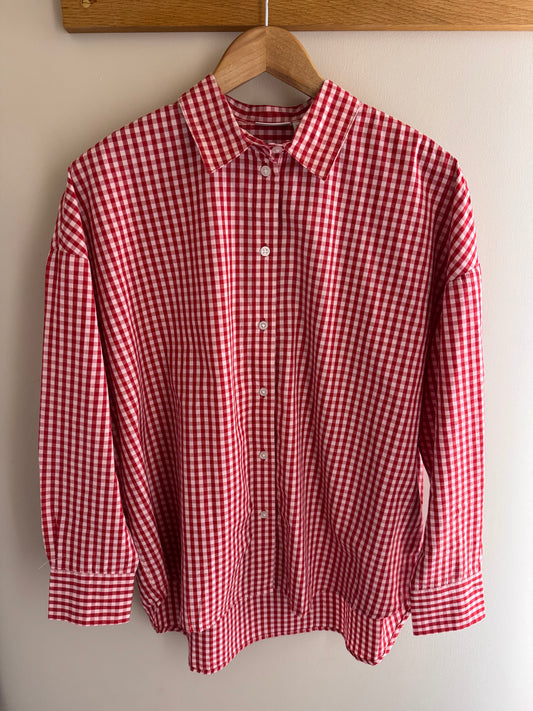 Red and white checkered shirt on a wooden hanger against a beige wall.