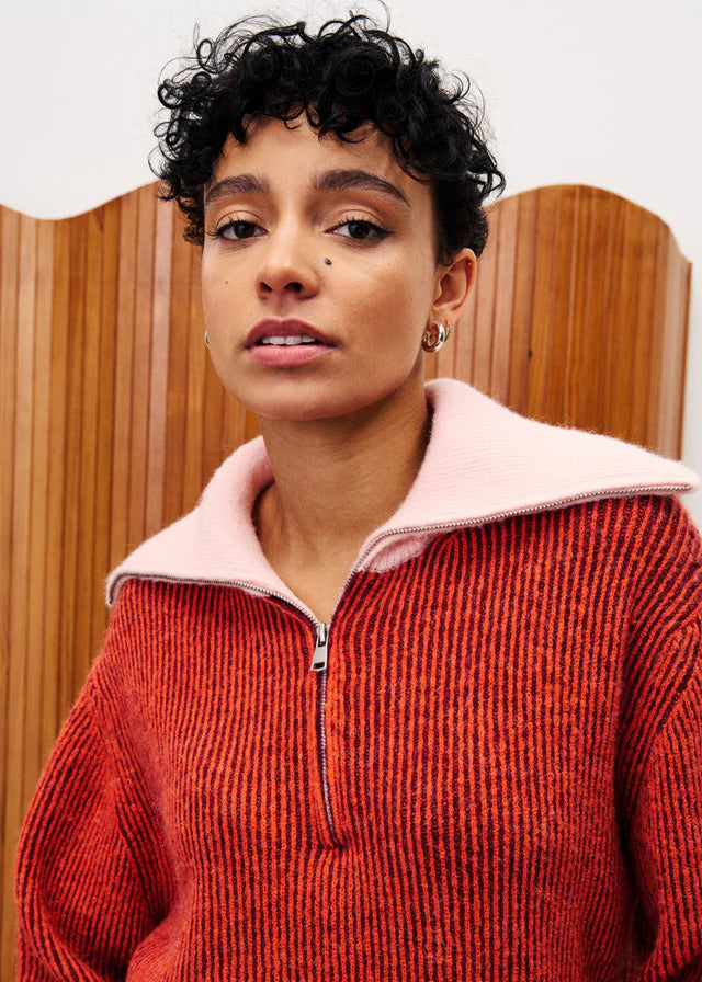 Person wearing a red sweater with a pink collar against a wooden background