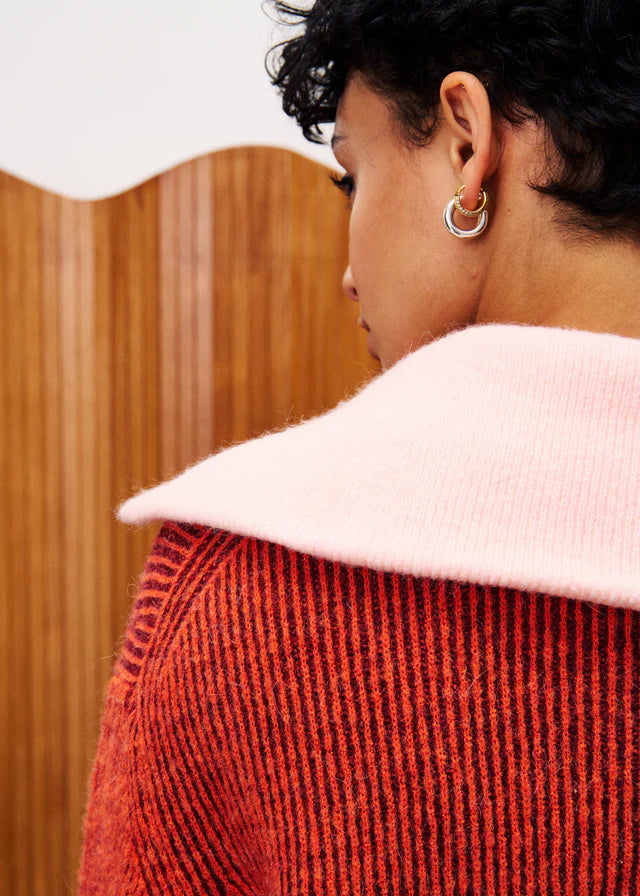 Person wearing a red textured sweater with a white collar, standing against a wooden wall.