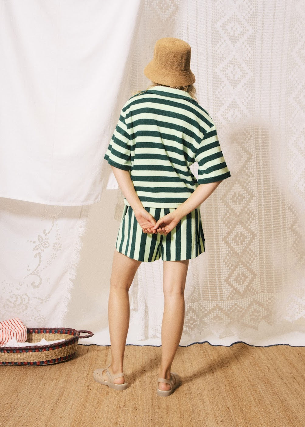 Person wearing a green and white striped outfit standing in front of a textured white wall.
