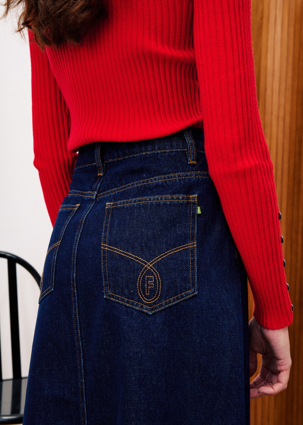 Person wearing a red sweater and dark blue jeans with a brand logo.