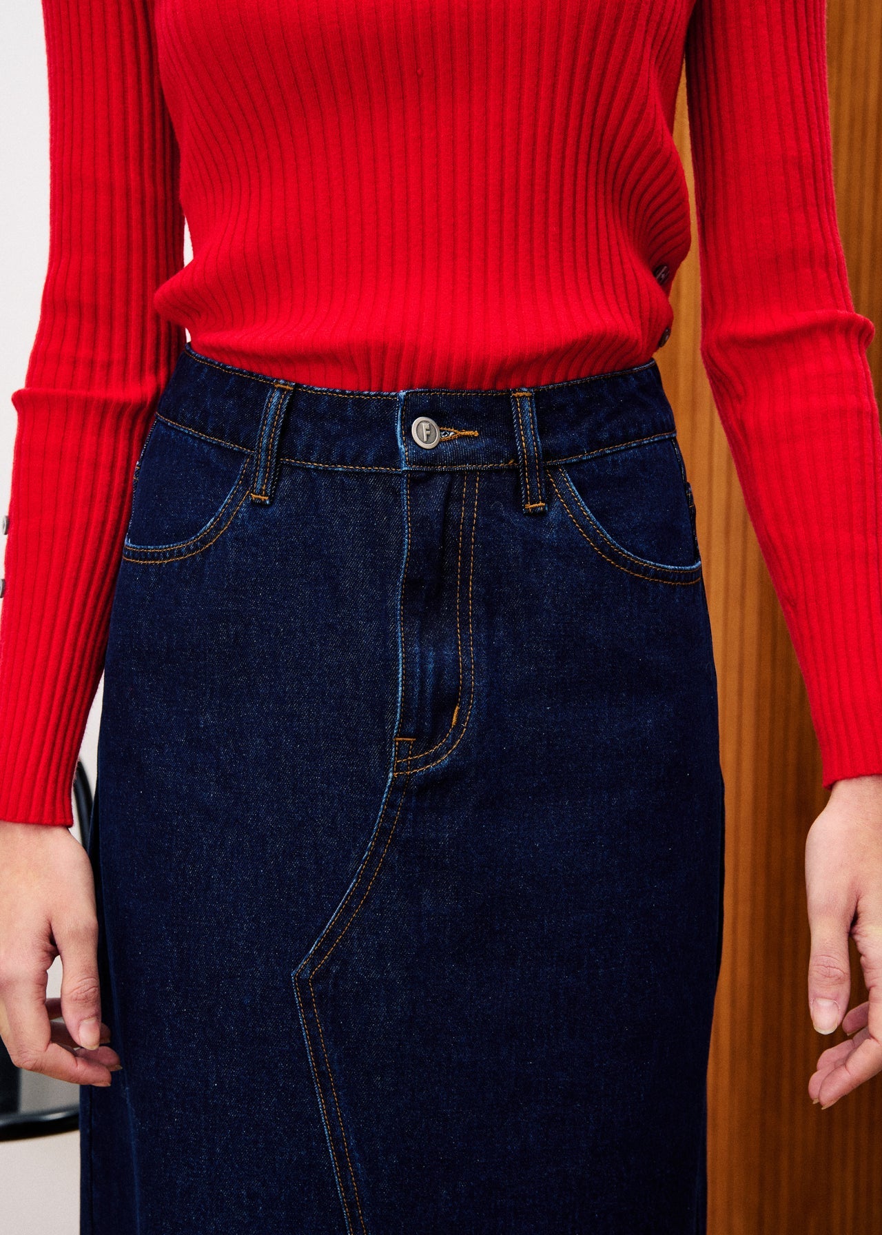 Person wearing a red ribbed sweater and dark blue jeans against a wooden background