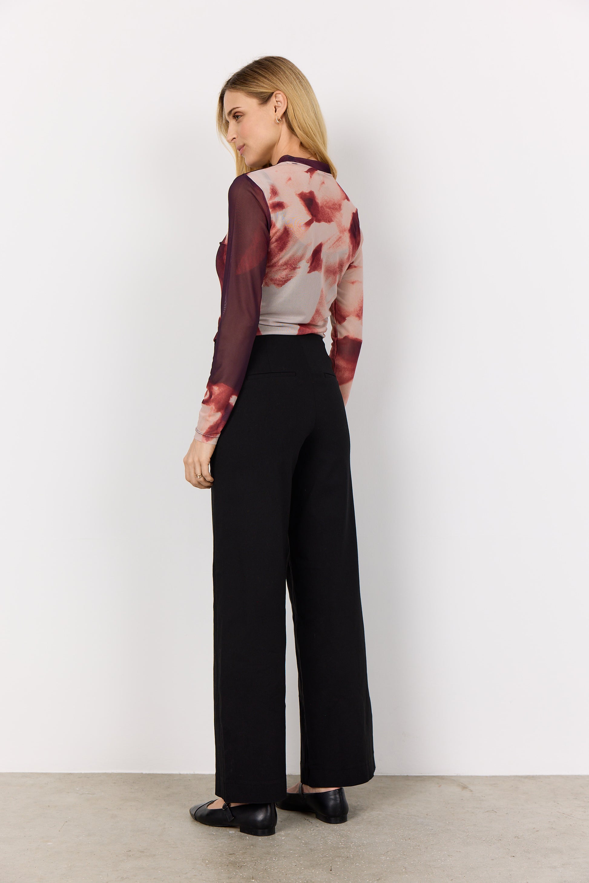 Woman wearing a patterned top and black pants against a white background