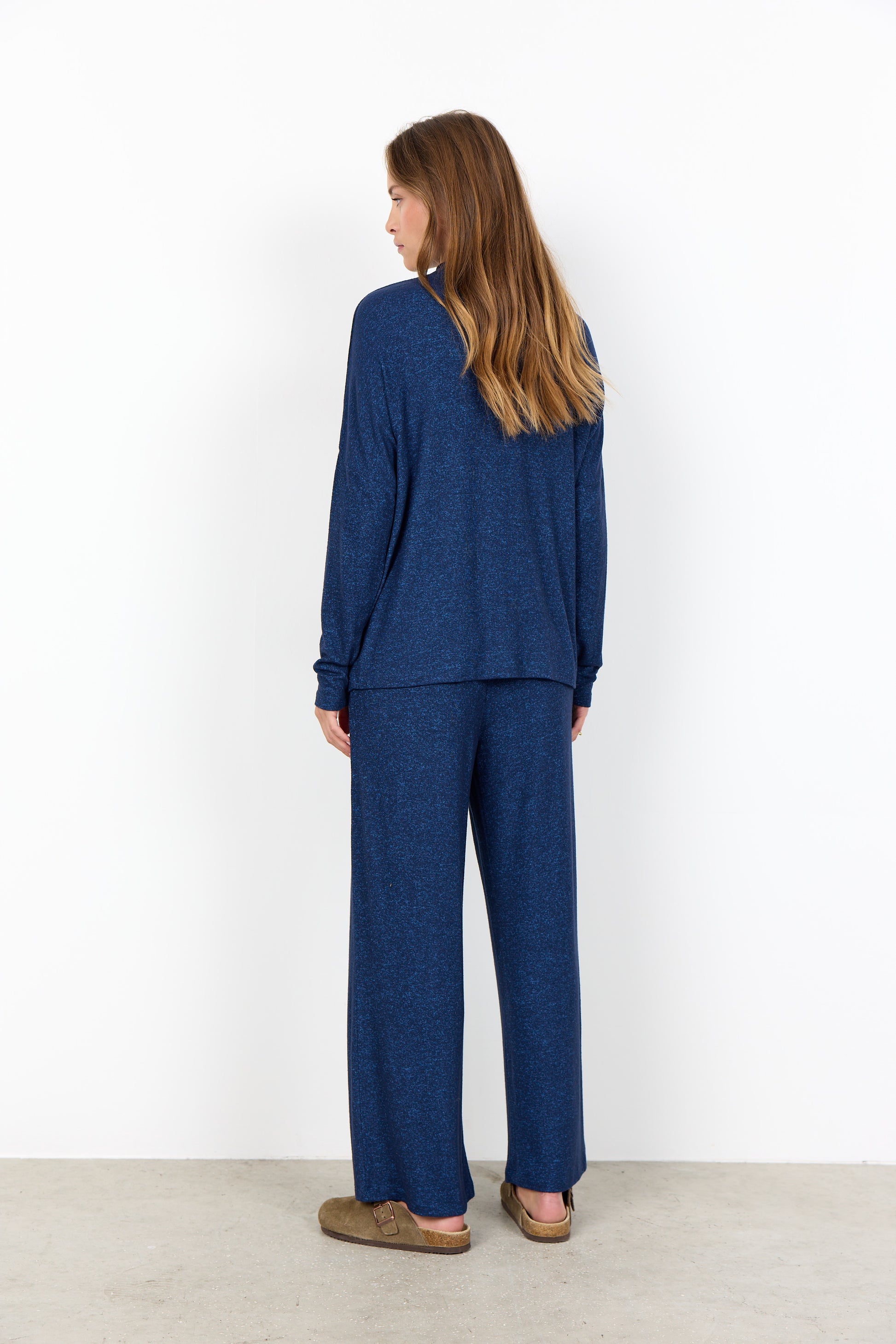 Woman wearing a blue outfit standing against a white wall