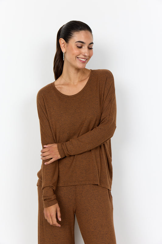Woman wearing a brown long-sleeve top and pants against a white background