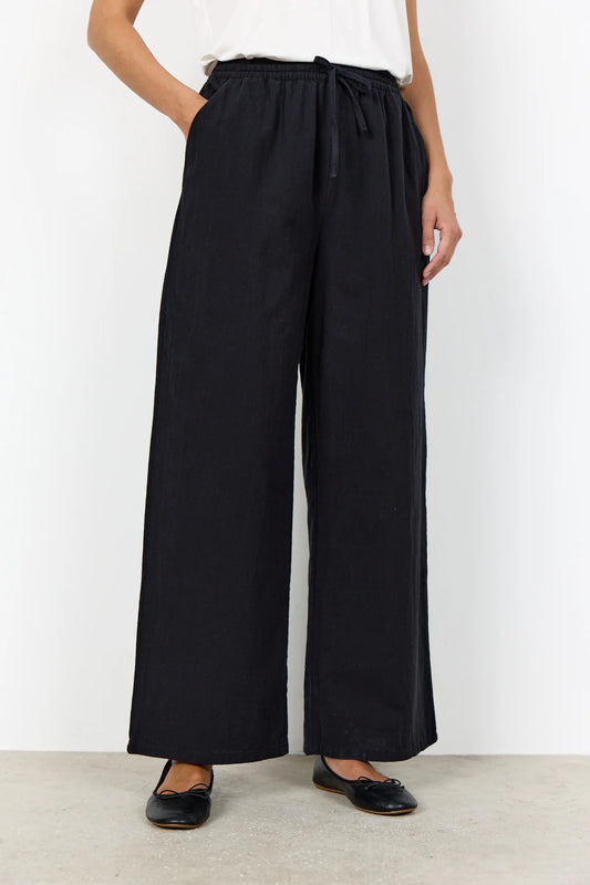 Person wearing black wide-leg pants with a white top on a plain background