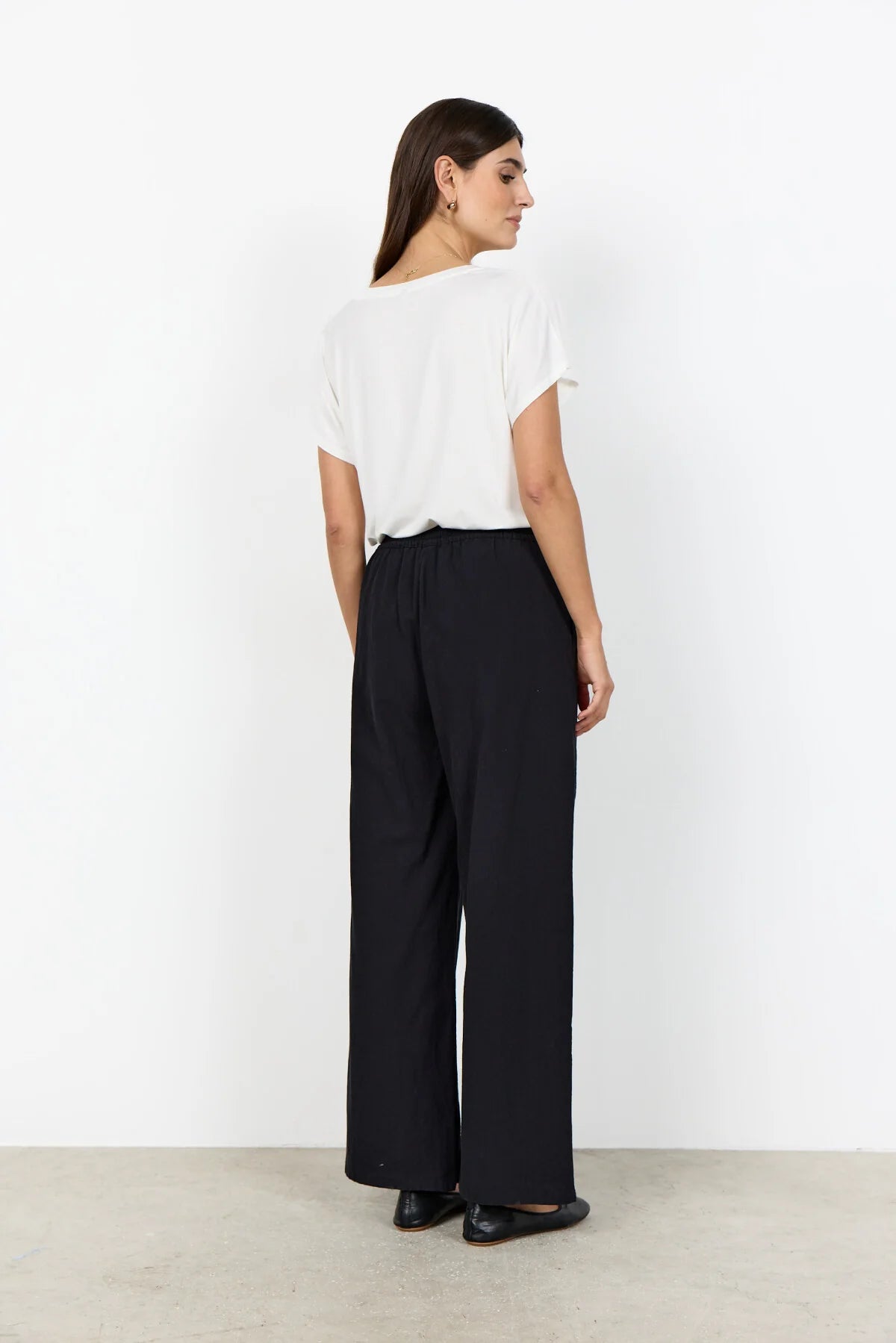 Woman wearing a white blouse and black high-waisted pants against a white background