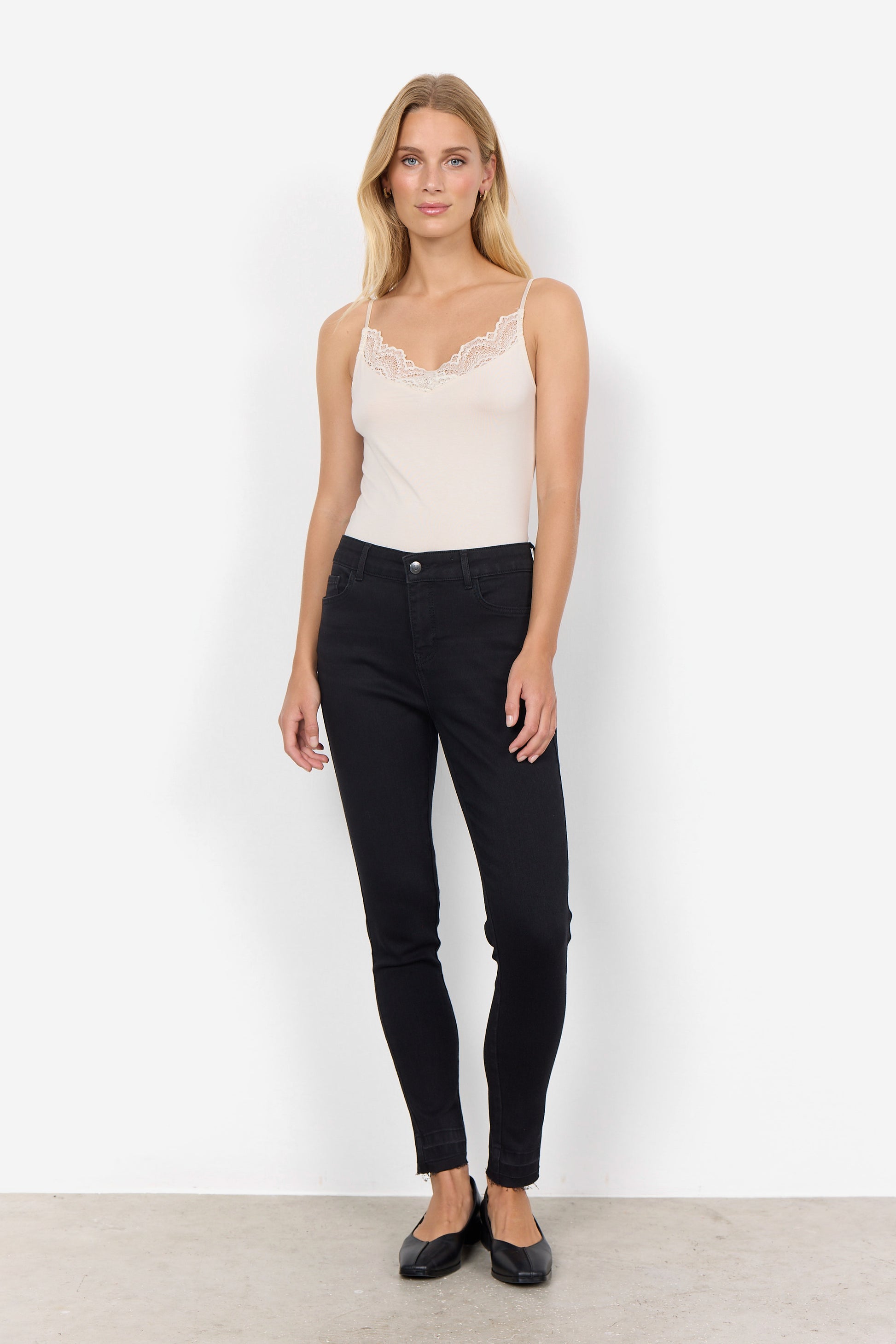 Woman wearing a beige lace top and black jeans on a white background